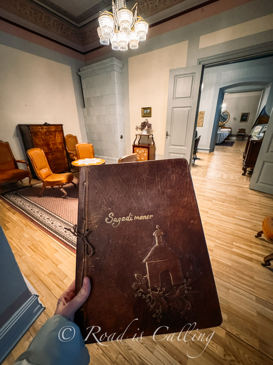my hand holding a book about Sagadi Manor in front of the old room in this manor