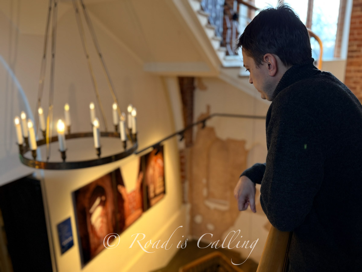 Man standing above stairwell looking down at candle-lit interior in University of Tartu Museum