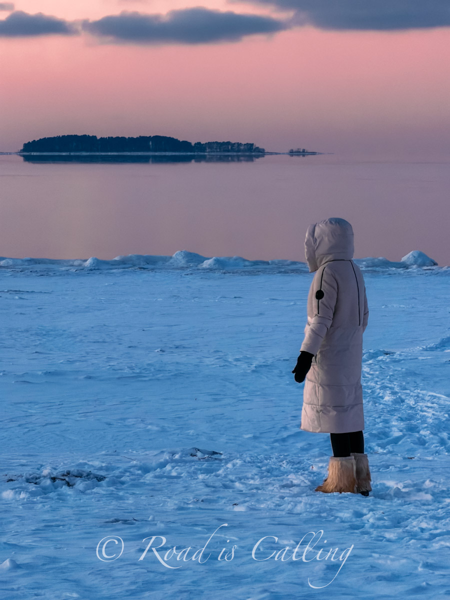 woman standing on frozen Baltic Sea at sunset in Lahemaa National Park