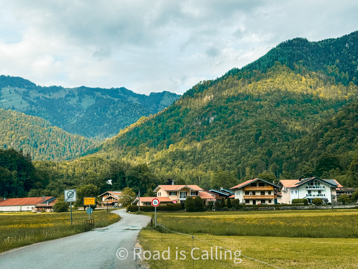 road through the Bavarian village leading toward green alpine mountains on a cloudy day