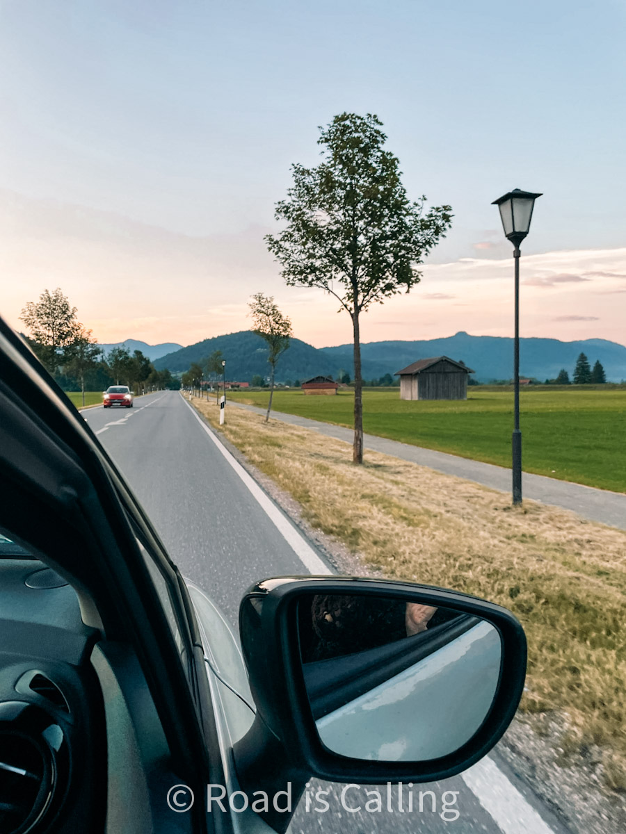 car driving on the road through the Bavarian countryside with open views of the Alps