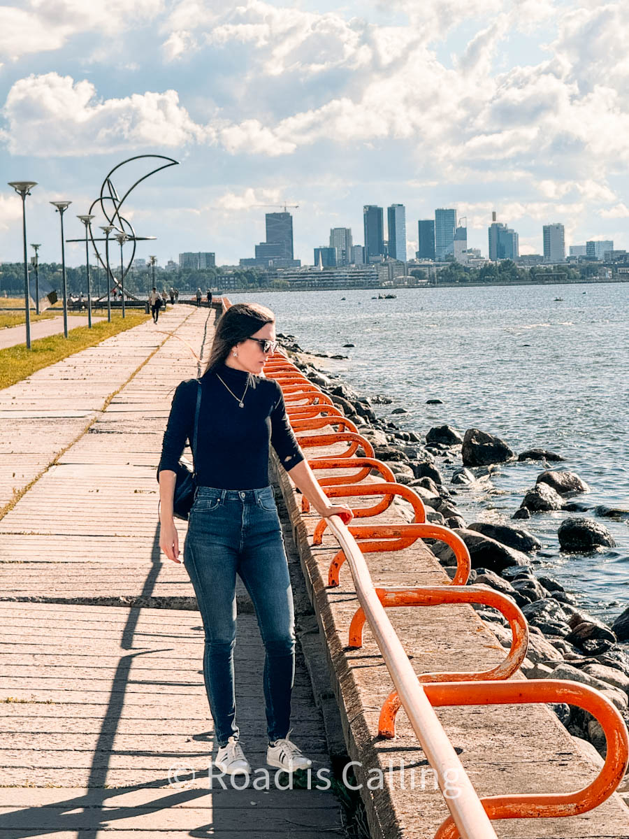 woman is standing on shore with Tallinn in the background