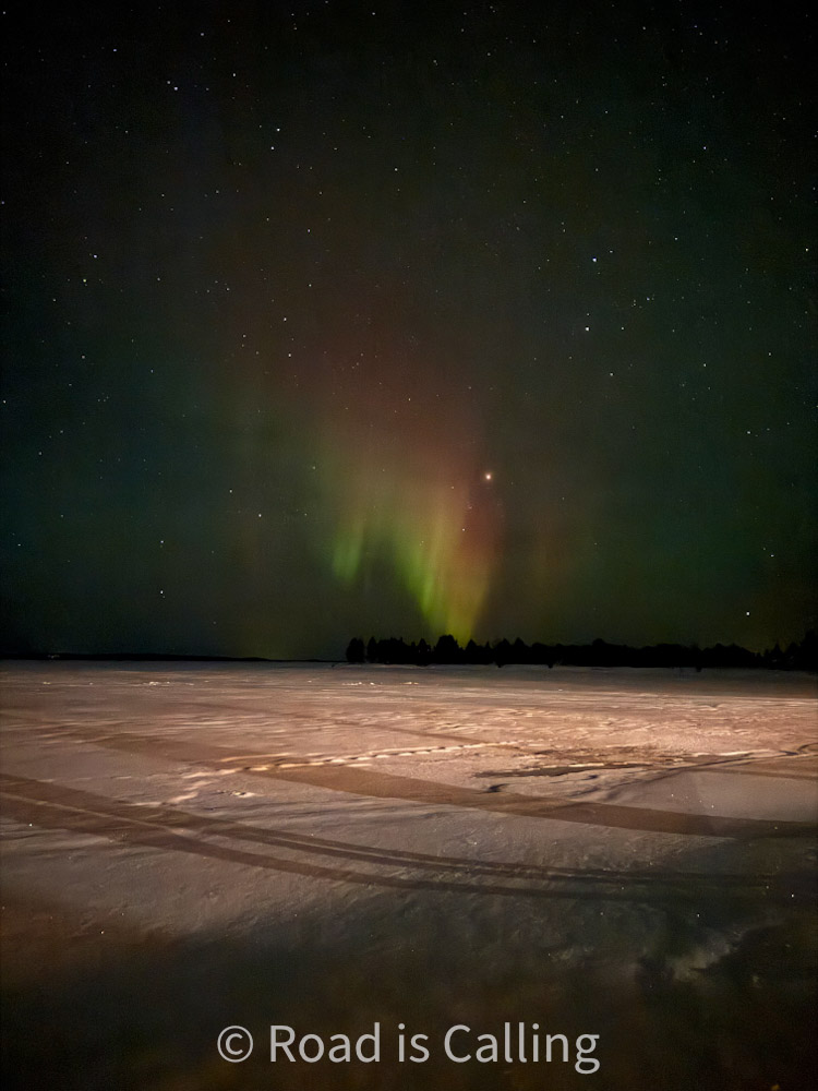 Northern lights in green and red over frozen snowy lake in Rovaniemi Lapland