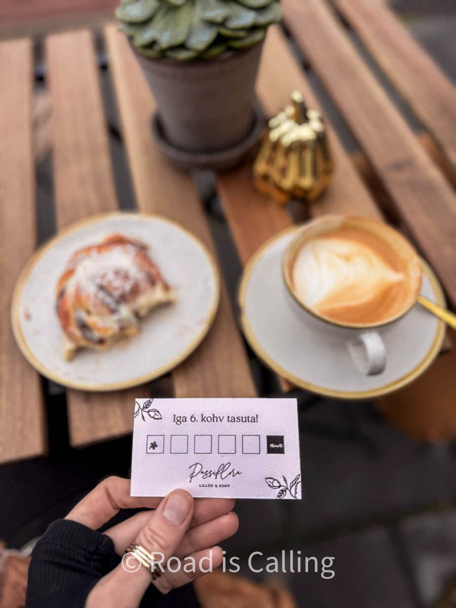 Hand is holding a coffee bonus card with a a cup of coffee and a cinnamon bun in the background