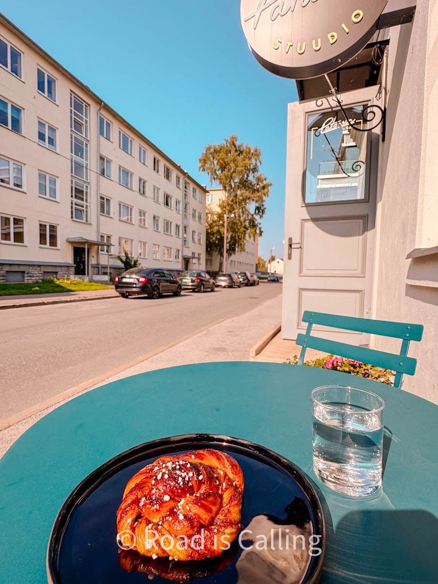 A cinnamon bun and a glass of water on a table outside on a sunny day