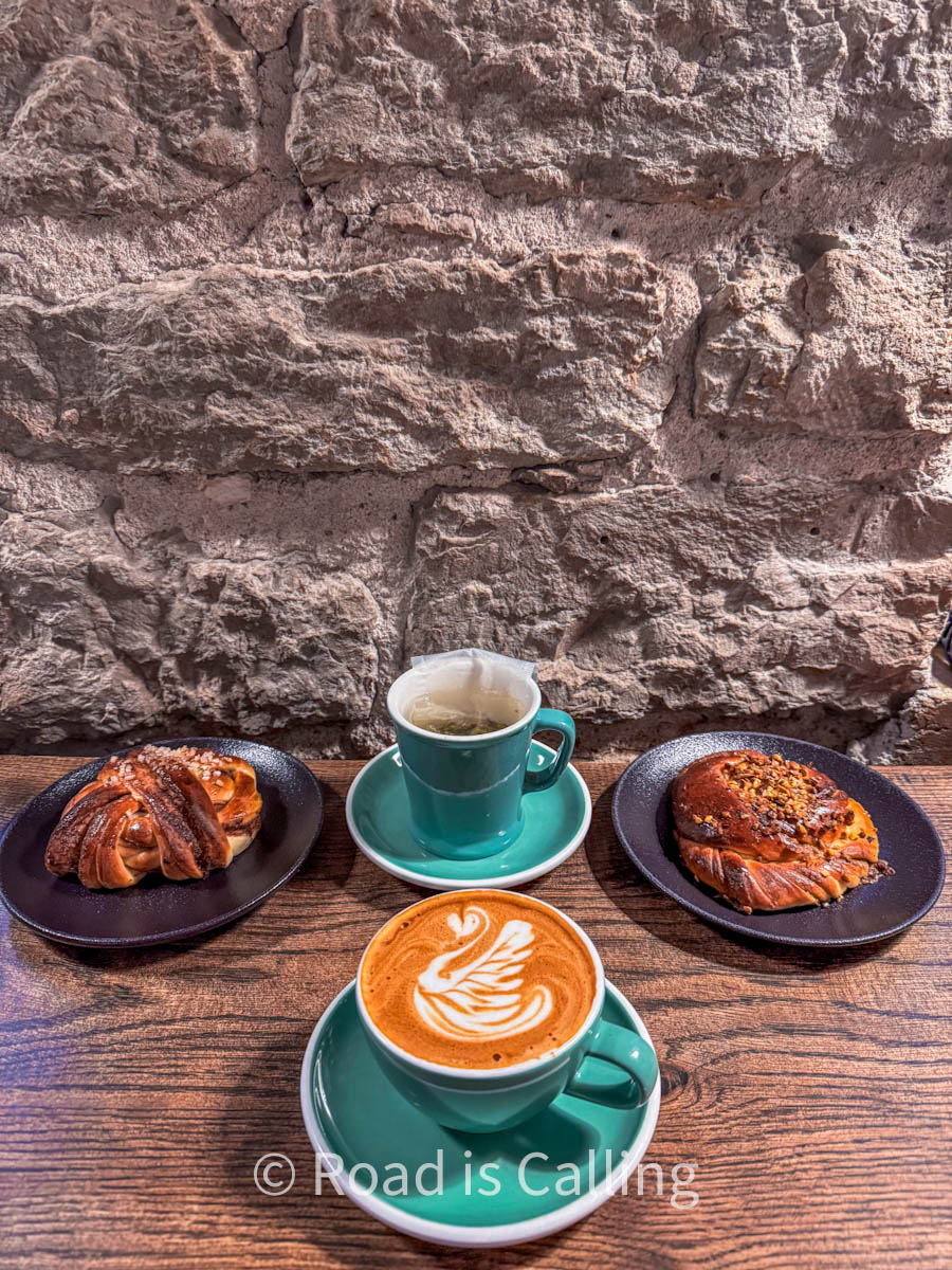 A couple of pastries and a cup of coffee and a cup of tea on the table by the stone wall