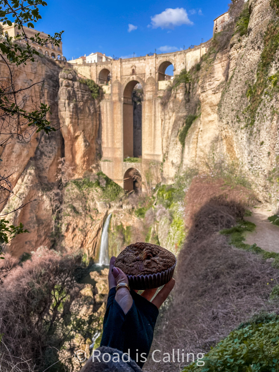 holding a muffin with a view of Puente Nuevo bridge in Ronda - a must-visit place in Europe in November