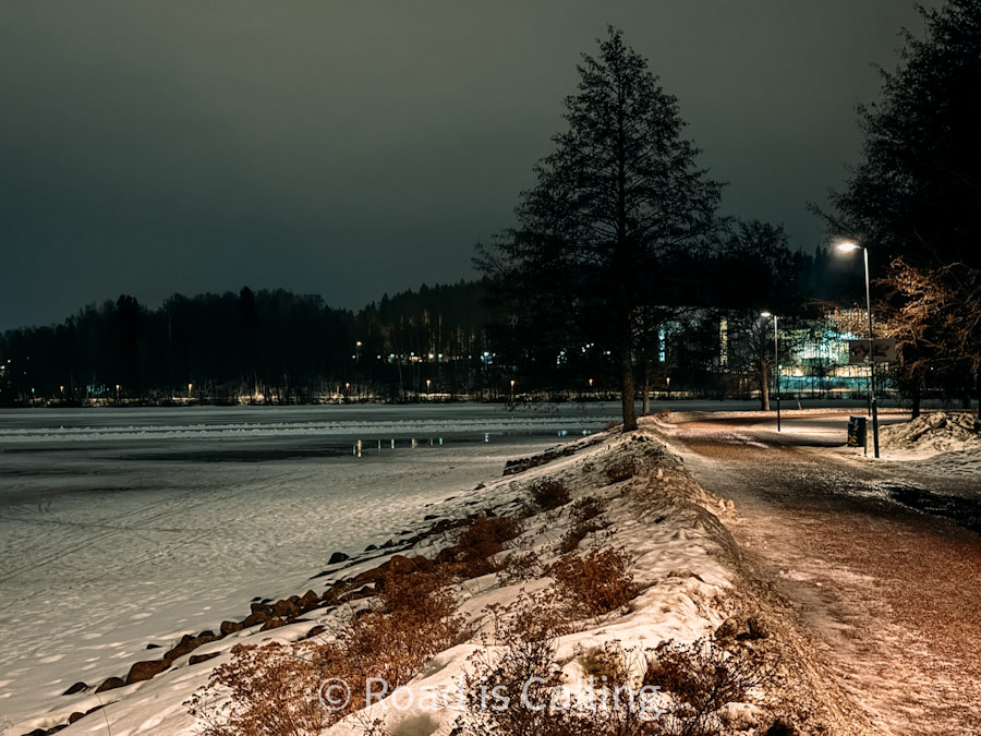 Snowy lakeside walking path illuminated by streetlights at night in Jyväskylä, Finland
