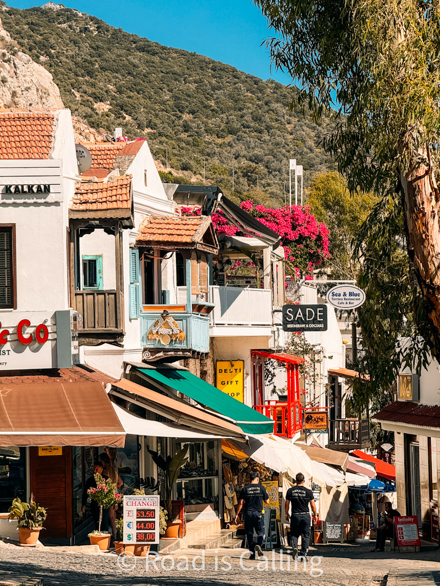 Lively street scene in Kalkan, Turkey with colorful shop signs, cafes, and traditional architecture against a mountain backdrop