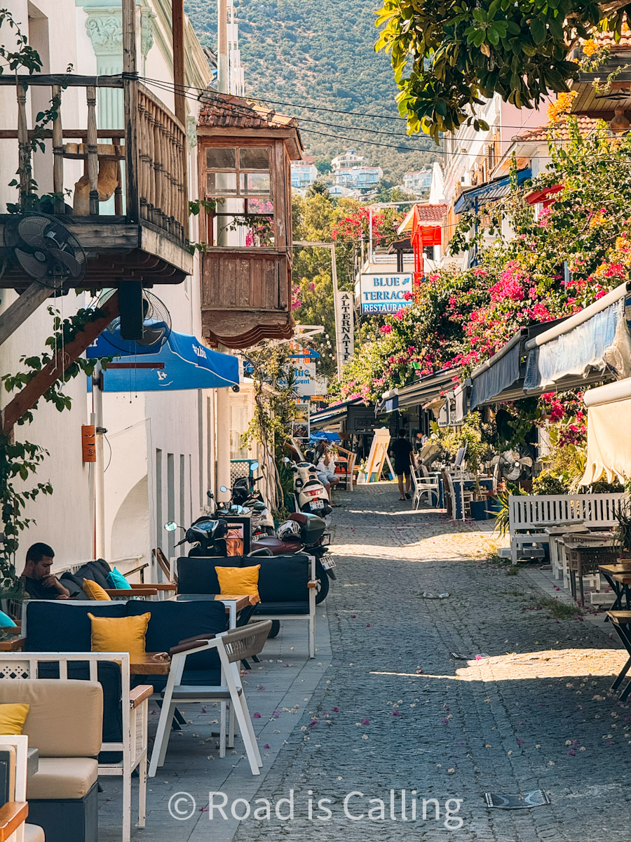 Charming narrow street in Kalkan lined with outdoor seating, scooters, and blooming bougainvillea