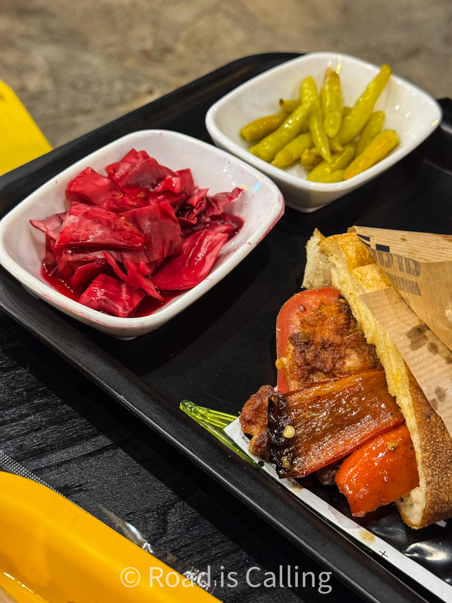 Turkish street food tray with a sandwich stuffed with grilled vegetables, served with pickled cabbage and green peppers