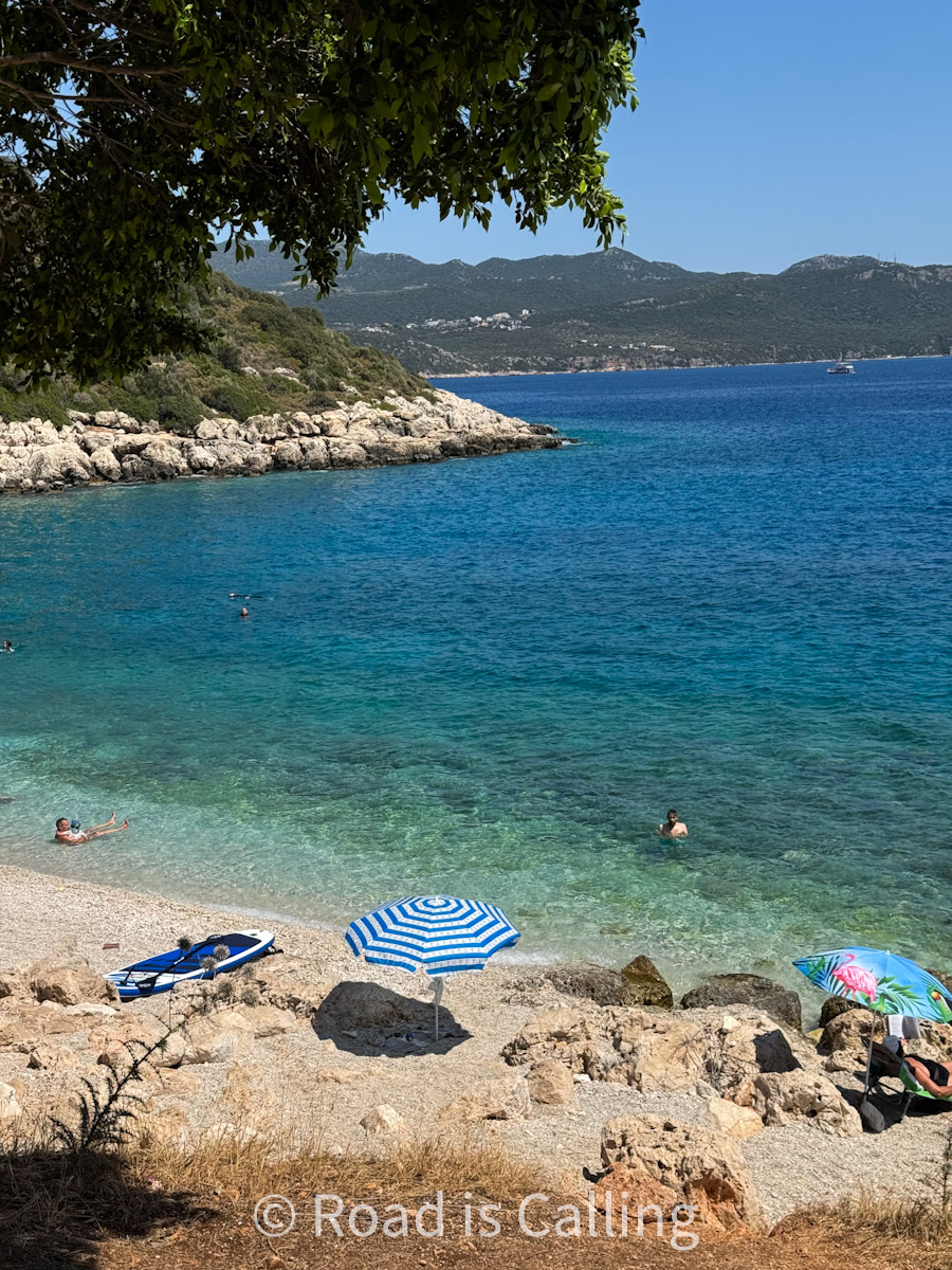 Quiet pebble beach in Kaş, Turkey with turquoise water, rocky coastline, and striped beach umbrellas
