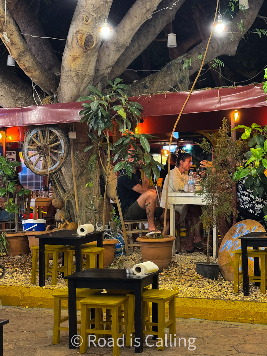 Cozy outdoor restaurant in Kaş, Turkey, with tree-shaded seating, small tables, and a warm evening atmosphere