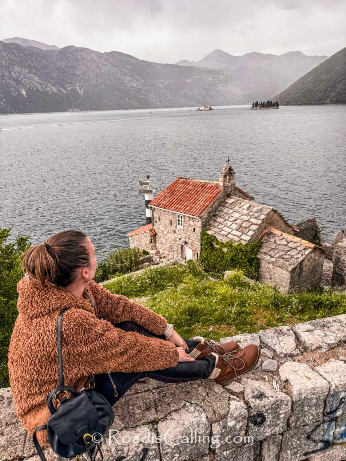 girl sitting on the wall above old church by adriatic sea in Kotor Bay in autumn