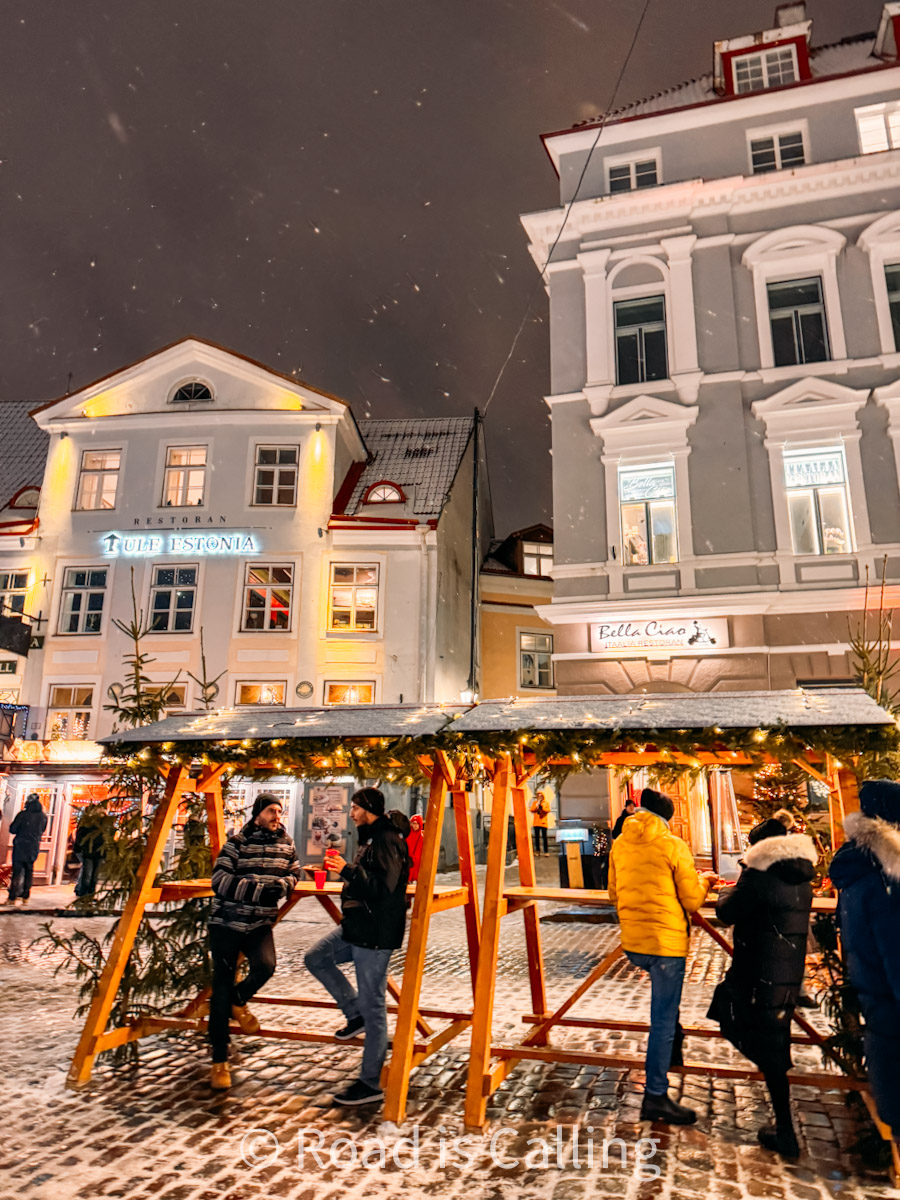 People enjoying Tallinn Christmas market at Town Hall Square under festive lights and wooden stalls