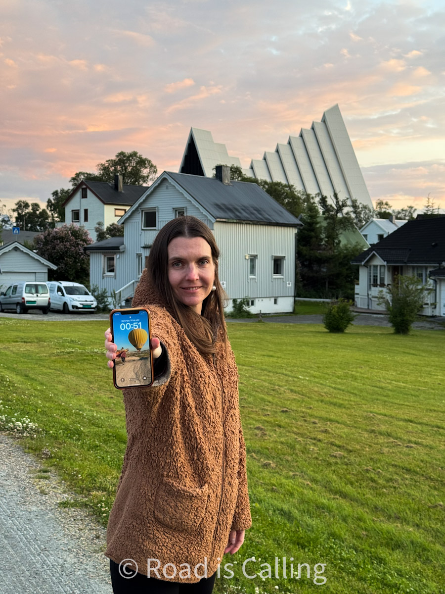 Me showing a phone time at midnight in front of Tromsø's Arctic Cathedral during the midnight sun in July