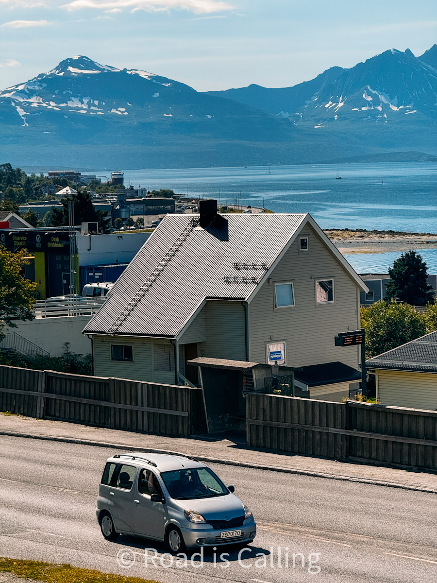 Coastal house along main road in Tromsø with mountain peaks and fjord in the background under bright sun