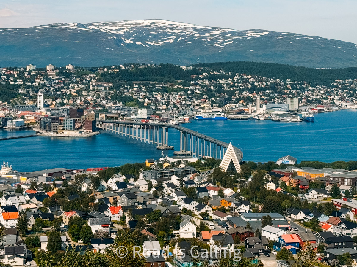 Panoramic view of Tromso with the iconic Tromsø Bridge, Arctic Cathedral, and snow-capped mountains across the blue fjord
