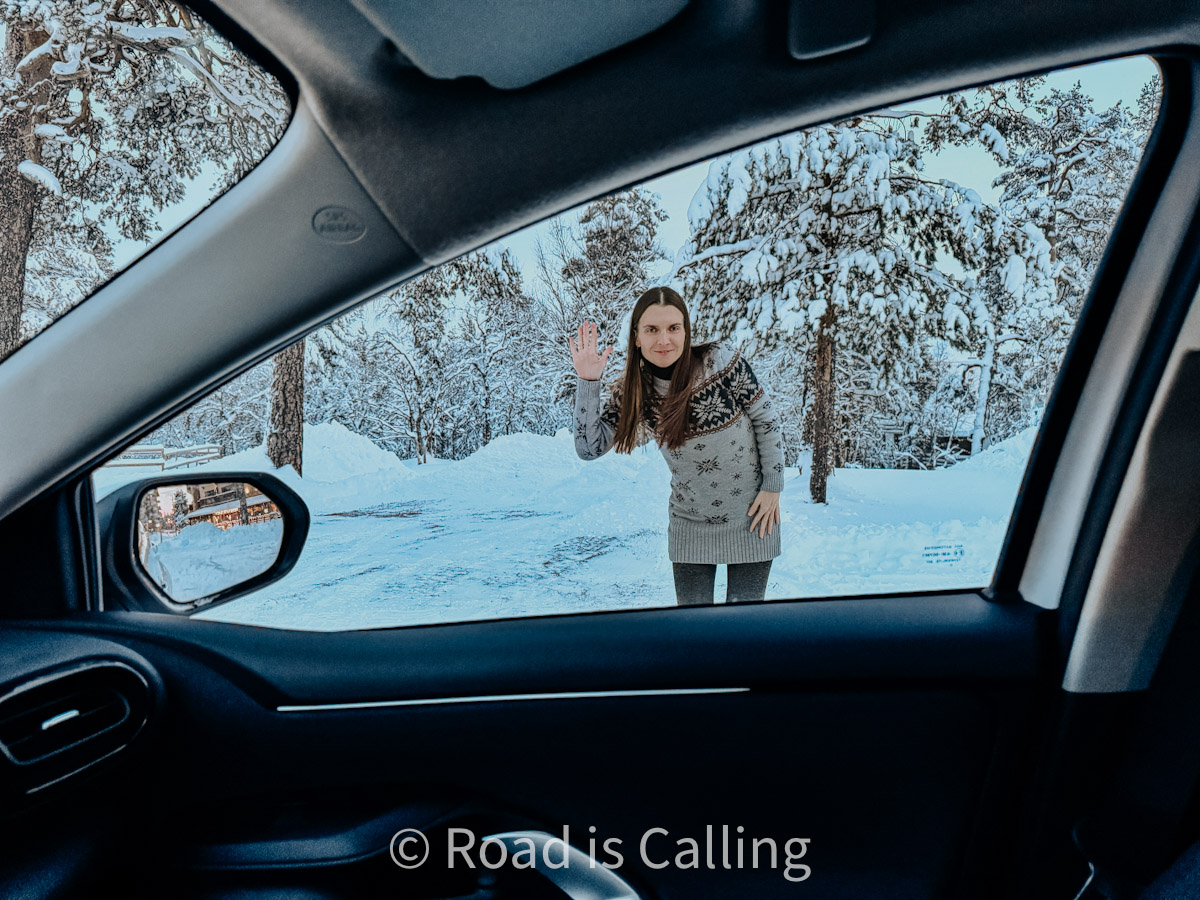 Woman waving outside a car in a snowy forest in Finnish Lapland