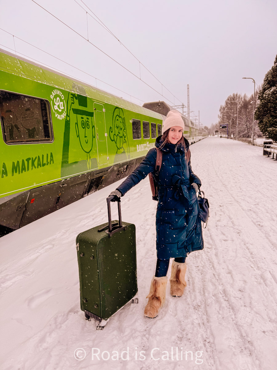 Traveler with suitcase standing by a green VR train in snowy Finland