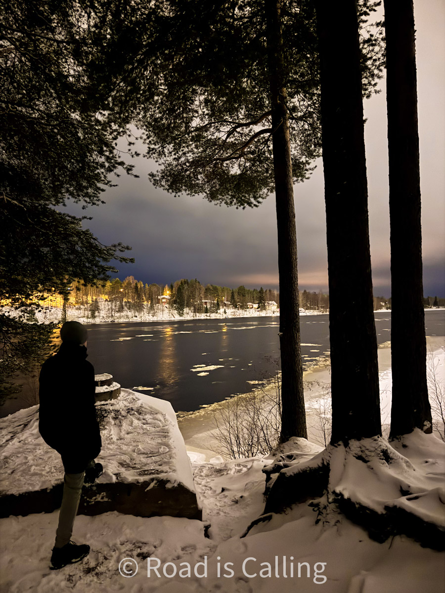 Person standing by a snowy riverbank at dusk in Finnish Lapland in November