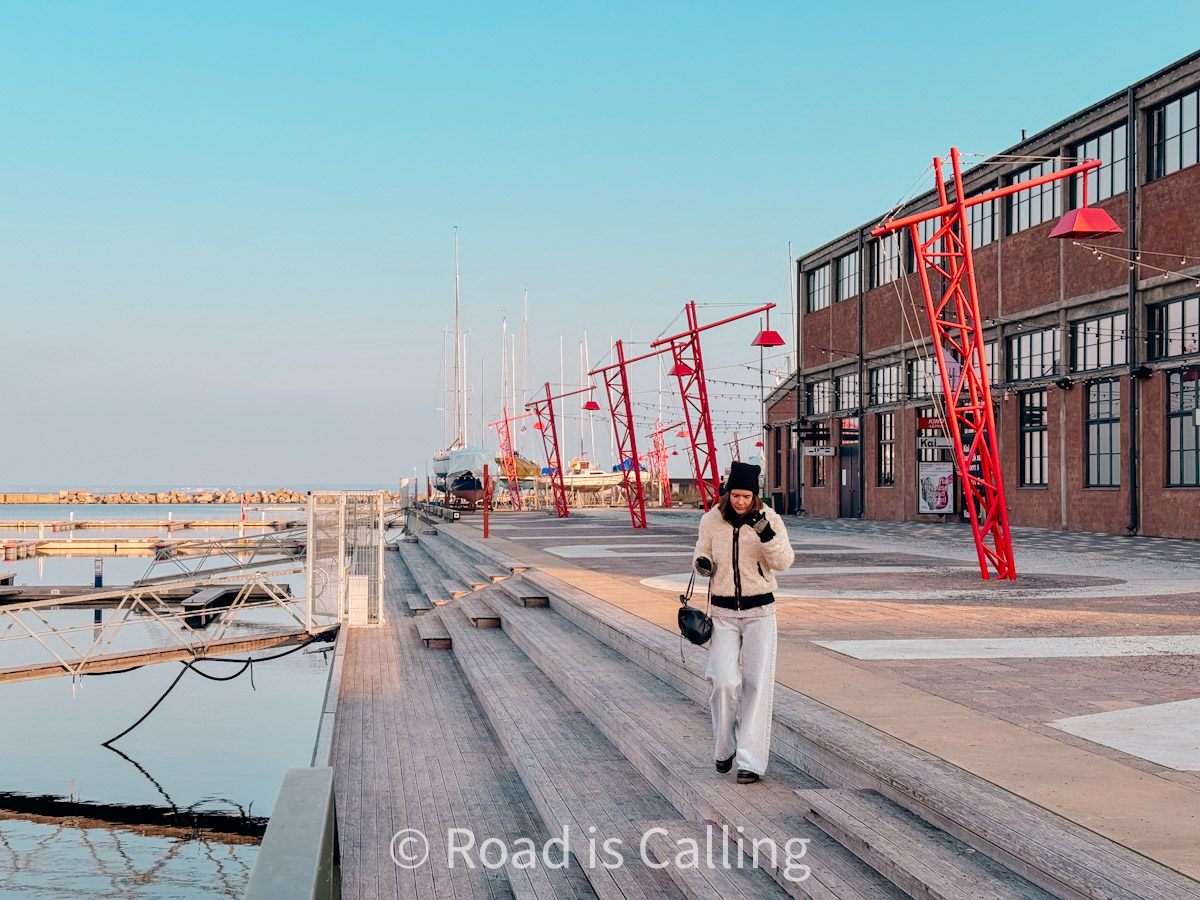 Woman walking past red cranes on Noblessner marina boardwalk in Tallinn during a sunny winter morning