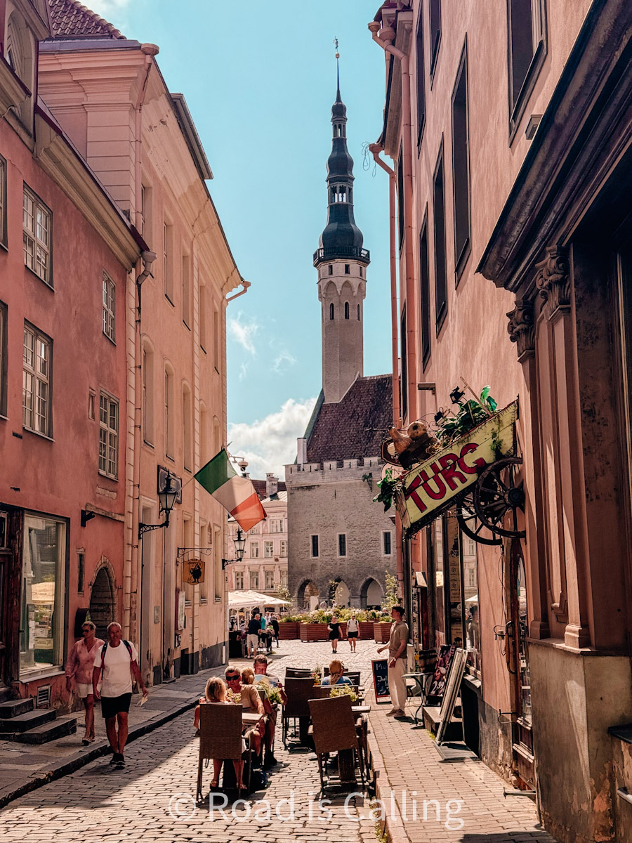 Colorful street in Tallinn Old Town with outdoor cafes and view of Town Hall tower in the background