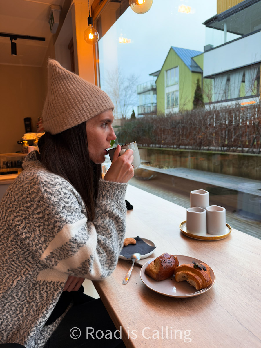 Woman sipping coffee inside a cozy café in Tallinn with pastries on the table and large window view