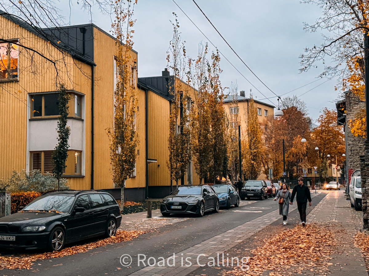 Couple walking down a quiet street lined with yellow buildings and autumn leaves in Tallinn’s Kalamaja district