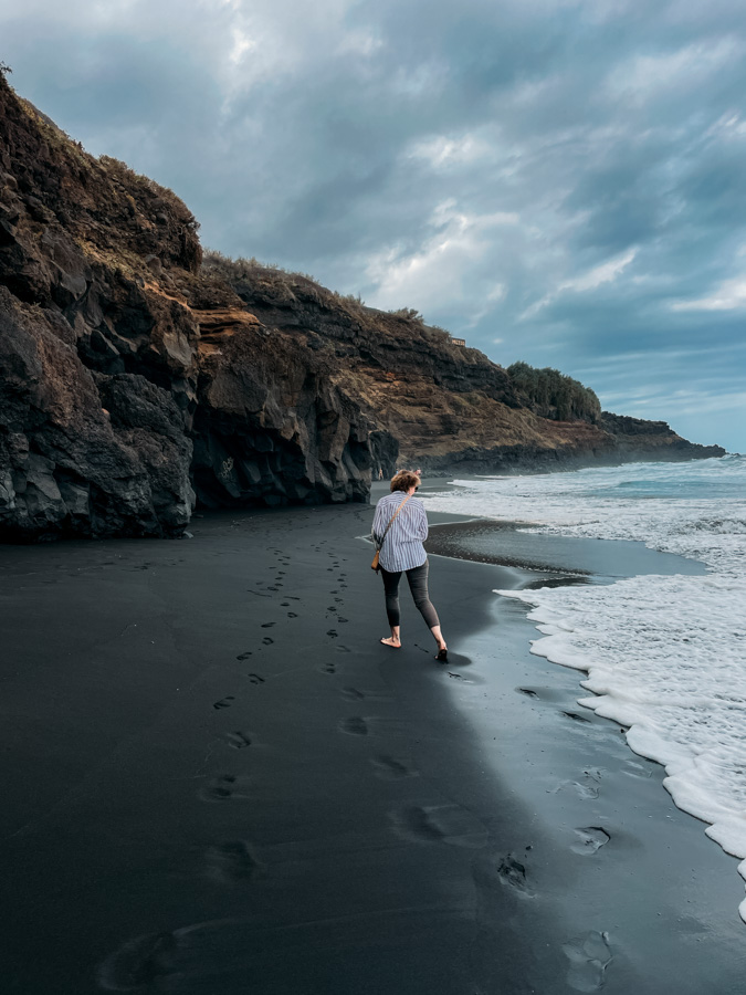 winter on a volcanic black sand beach in the Canary Islands with waves, cliffs, and dramatic winter sky